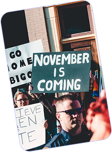 Protesters holding signs including one that reads 'NOVEMBER IS COMING' and others partially visible in a crowd.